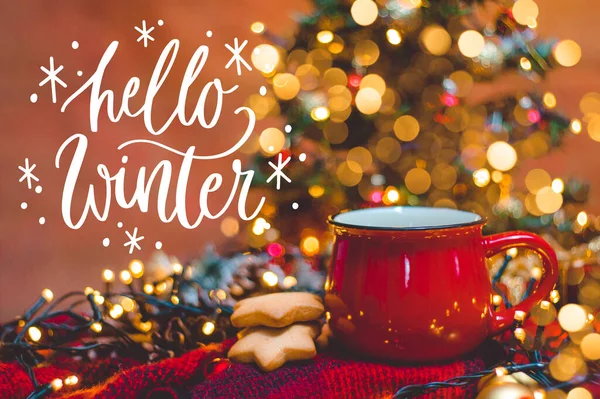 Kırmızı fincan sıcak kahve, Noel ışıkları, taze kurabiyeler, krema, tarçın ve saman.