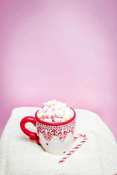 Red mug with marshmallows and winter ornaments on a white sheets