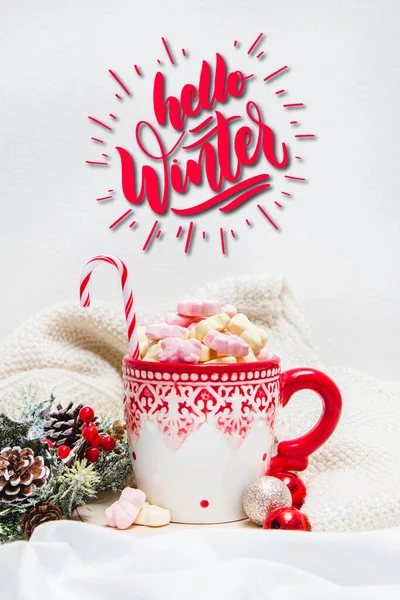 Red mug with marshmallows and winter ornaments on a white sheets