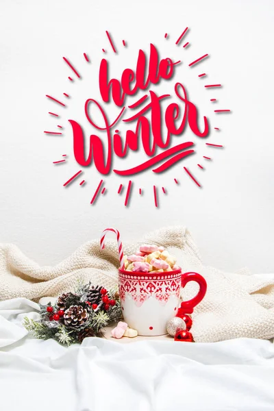 Red mug with marshmallows and winter ornaments on a white sheets