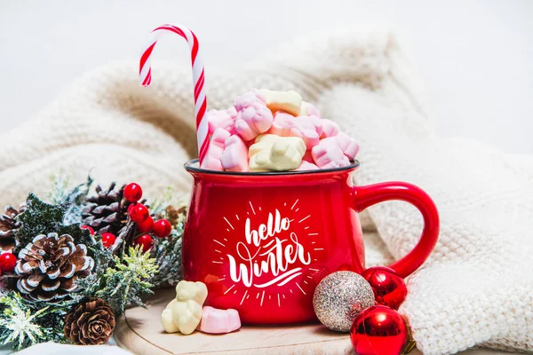 Red mug with marshmallows and winter ornaments on a white sheets