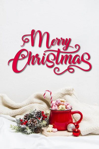 Red mug with marshmallows and winter ornaments on a white sheets