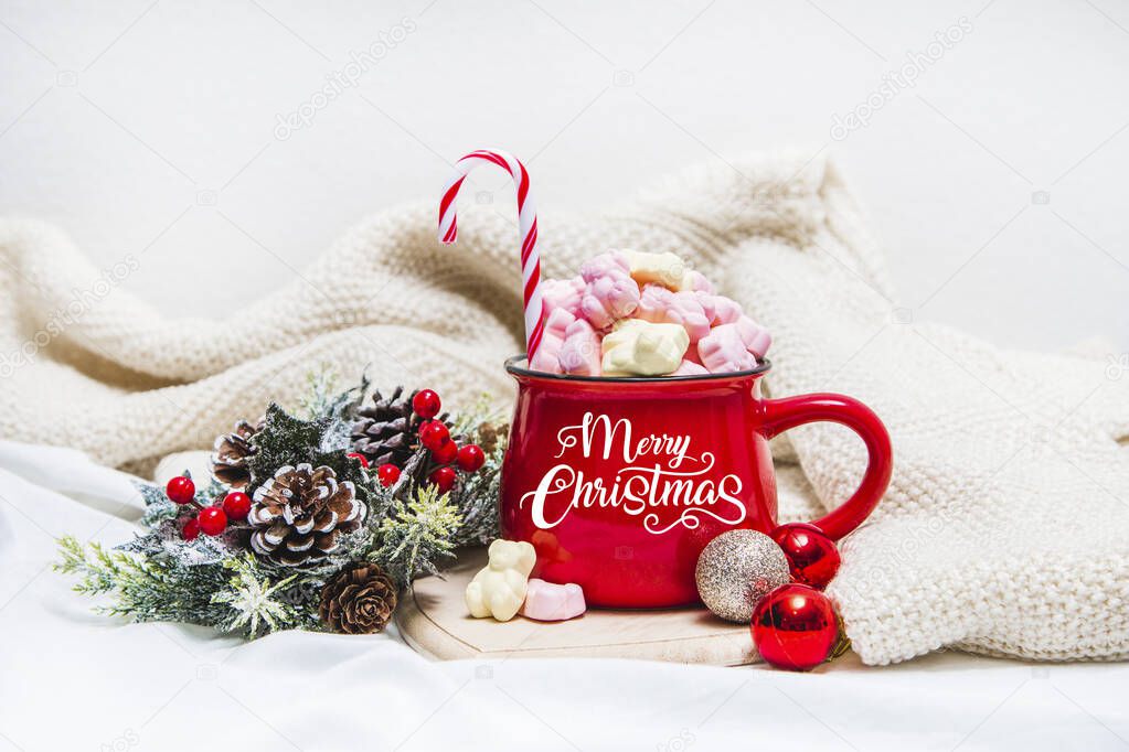 Red mug with marshmallows and winter ornaments on a white sheets 