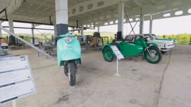 Retro beyaz ve yeşil motosiklet ve otomobil kırsalında sergisinde gölgelik altında notlar standlı