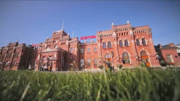 美丽的红色火车站大厦和绿色草在前景反对晴朗的蓝天 — 图库视频影像