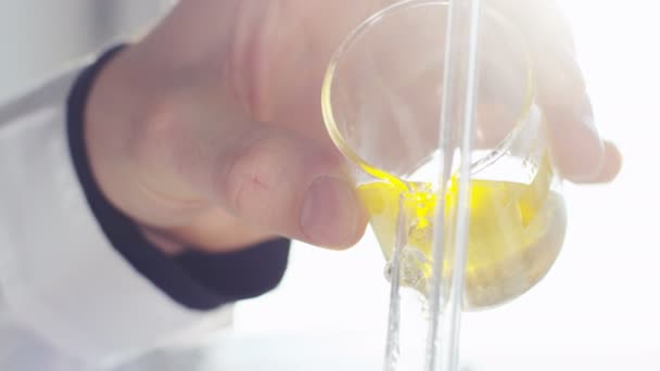 研究室助手のランプに対して長いグラスに注がれる原油から生成されるクローズ アップ黄色液体 — ストック動画