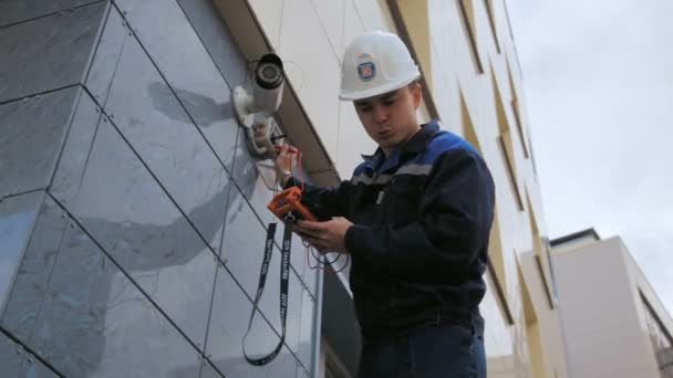 Trabajador ajusta videcam montado en la pared del edificio con el instrumento — Vídeo de stock