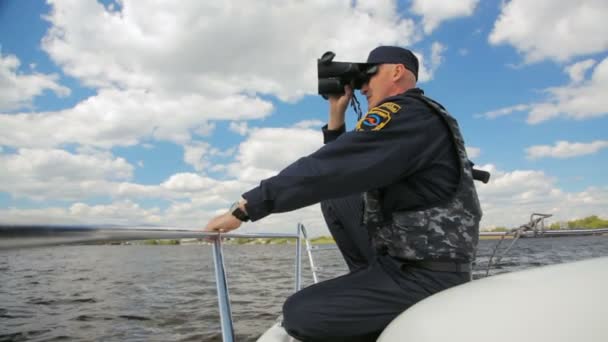 Νερό αστυνομικός κάθεται στο μηχανοκίνητο σκάφος παρακολούθηση ποτάμι μέσα από κιάλια — Αρχείο Βίντεο