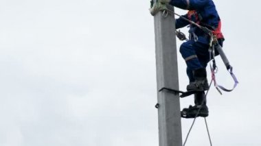 Kazan, Tataristan Rusya - 28 Mayıs 2018: Beton yüksek gerilim direk bacak-ütüler 28 Mayıs kazan gri gökyüzü karşı kullanarak özel kıyafet içinde Closeup işçi elektrikçi tırmanıyor