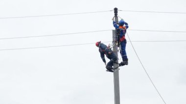 elektrikçi uzanıyor ve meslektaşım tel bacak-ütüler kullanarak kutup üzerinde düzeltmeler
