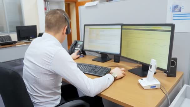Jovem empregado trabalha na frente de telas de computador no escritório — Vídeo de Stock