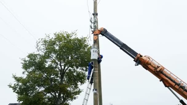 Werknemer installs transformator naar pole op de ladder — Stockvideo