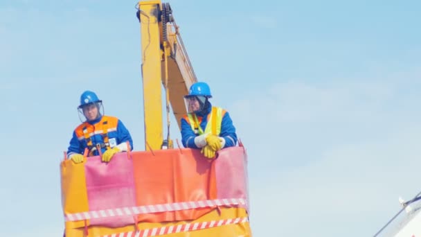 Hombres en cascos de pie en la grúa colgante de la cuna — Vídeos de Stock