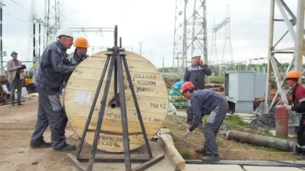 Trabajadores desenrollan cable de bobina en subestación eléctrica — Vídeo de stock