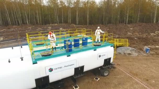 Travailleurs en tenue regarder dans l'écoutille sur réservoir avec des produits chimiques par la forêt de bouleau — Video