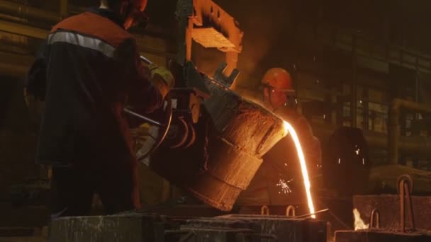 Liquid metal flow falls down and workers controlling process — Stock Video