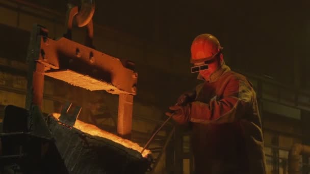 Man in mask mixes molten metal poured from bucket — Stock Video