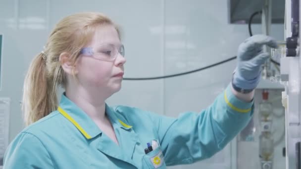 Blondine mit Brille und Handschuhen experimentiert im Labor an Gerät — Stockvideo