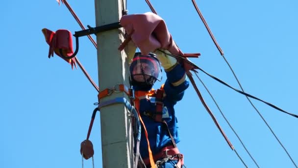 Werknemer werkt met elektrische draden op post onder de blauwe hemel — Stockvideo