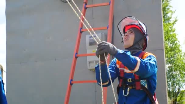 Competitor in outfit looks upward pulls rope against ladder by wall — Stock Video