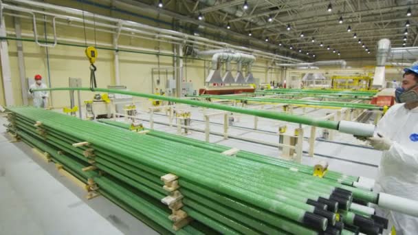 Рабочие контролируют подъем зеленых труб с помощью кранового крючка в современном цехе — стоковое видео