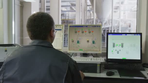 Ingeniero se sienta frente a pantallas de computadora contra taller de producción — Vídeos de Stock