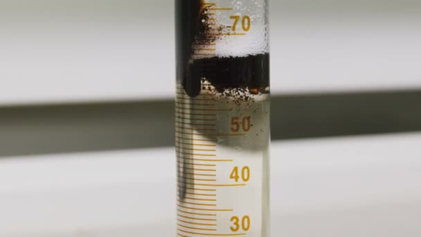 Масло льется в емкость, плавает на прозрачной жидкости в лаборатории — стоковое видео