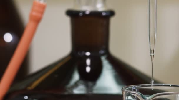 Cerrar goteo de líquido que sale de la gota de pipeta que se mantiene en la punta de la botella negra — Vídeo de stock