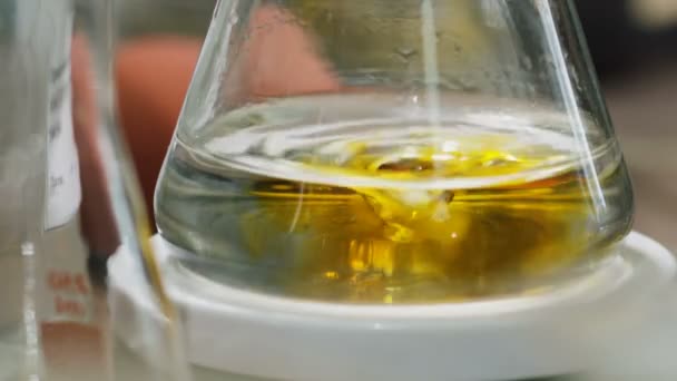 Baňka se otočí na stojanu bezbarvé kapaliny nezbarví žlutě s přidaný pramínek v laboratoři — Stock video