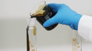Mavi kauçuk eldiven closeup bilim adamı elinde ham petrol işyerinde az su ile boyutlu yüksek kabı içine dökülen