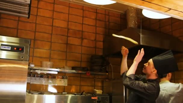 Guy chief in zwarte worpen van pizza deeg in café keuken — Stockvideo