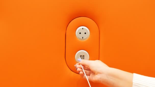 Chica conecta el teléfono inteligente al puerto de carga USB en la pared naranja — Vídeo de stock