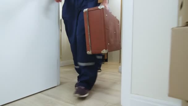 Lader trägt alten großen braunen Koffer in Raum mit Kisten — Stockvideo