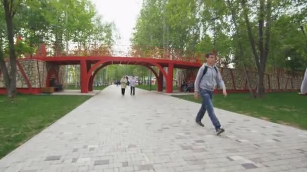 Moto lungo il parco primaverile oltre le persone sotto il ponte della bicicletta — Video Stock