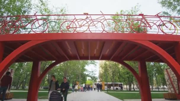 Ciudadanos caminan a lo largo del parque bajo el puente con pasamanos bicicleta — Vídeos de Stock