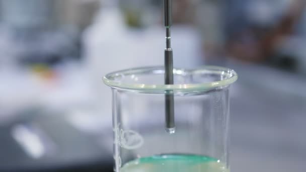 Close view metal tube put into clear slime in lab beaker — Stock Video