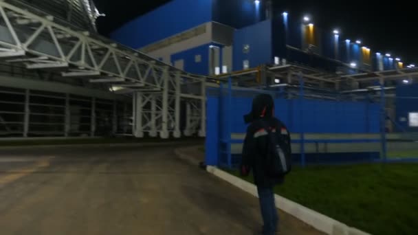Backside worker walks to brightly lit cooling tower in dusk — Stock Video