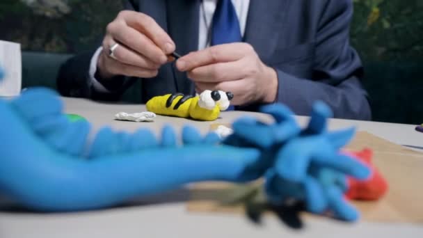 Крупный план человек делает пластилиновые полоски для игрушечной пчелы за столом — стоковое видео