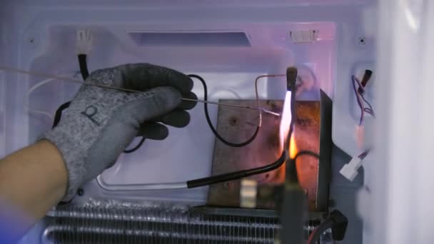 Работник сваривает металлические трубы для фреона внутри домашнего холодильника — стоковое видео