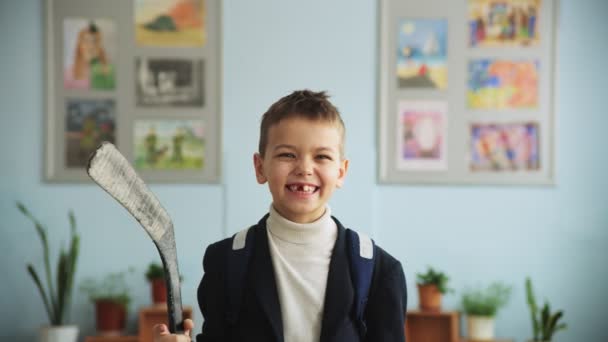 Boy without front tooth holds hockey stick in classroom — Stock Video