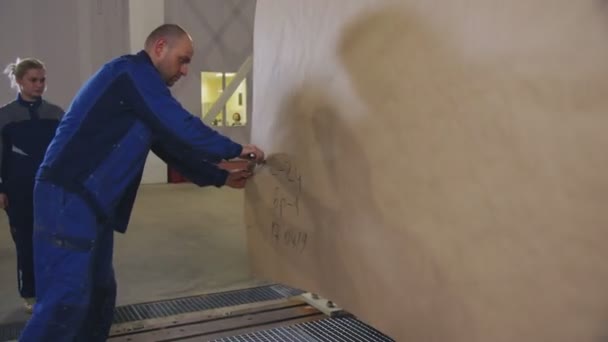 Worker in uniform cuts piece of paper in plant warehouse — Stock Video