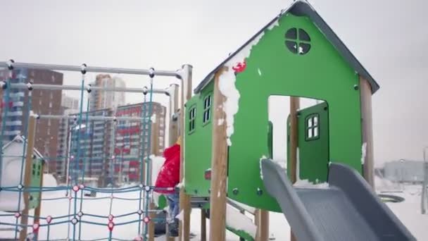 Criança em slides jaqueta vermelha no parque infantil no parque de inverno nevado — Vídeo de Stock