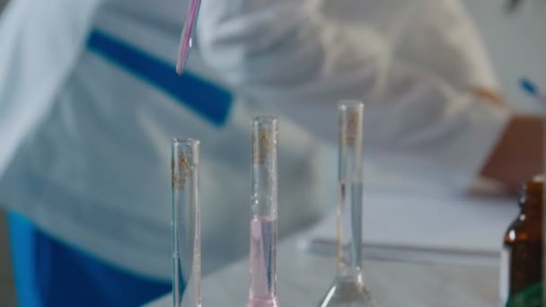 Lab assistant drops reagent into flask with liquid at table — Stock Video