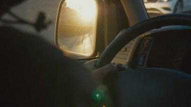 Adam gün batımında kalabalık cadde boyunca otomobil sürüyor.