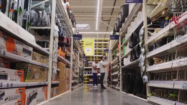 Jonge mannen kiezen gereedschap op planken op de moderne hardware markt — Stockvideo
