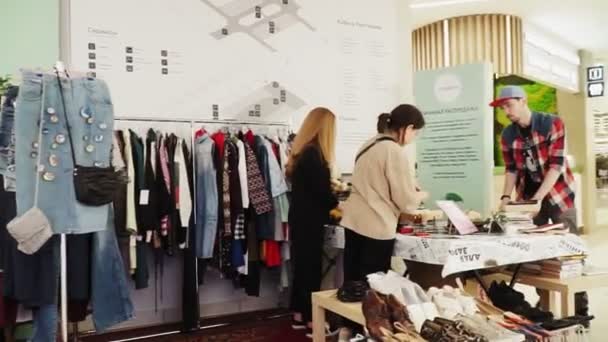 Tienda de moda con ropa en bastidores y vendedores en la mesa — Vídeo de stock