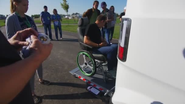 Man i rullstol rider ner från automatisk ramp nära van — Stockvideo