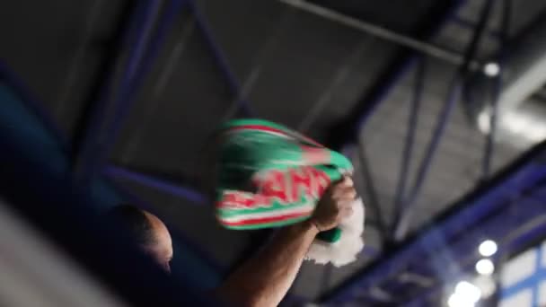 Лысый мужчина размахивает шарфом с логотипом команды на спортивной арене крупным планом — стоковое видео
