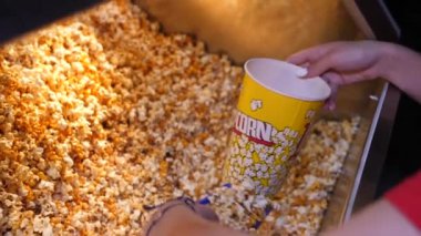 Kadın kafede sergilenen patlamış mısırla kağıt kovayı dolduruyor.