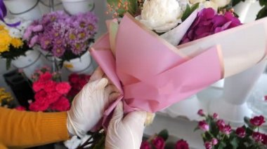 Çiçekçi dükkanında pembe folyoyla güzel buketler paketliyor.